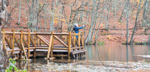 Asian woman taking selfie by mobile phone's camera in public park with winter clothes and blue coat on