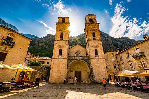 Kotor, Montenegro - July 24, 2016: Kotor  view showing Cathedral of Saint Tryphon with bell and clock tower, buildings, out door cafes and restaurants, rock mountains, trees, houses and people can be seen on the background in the Old town square area
