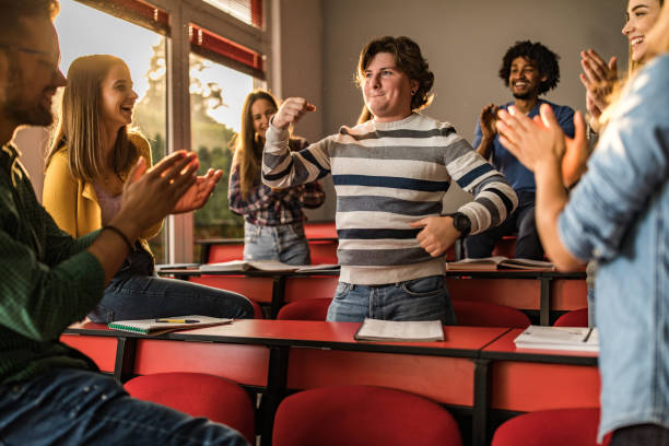 jóvenes estudiantes aplaudiendo a su amigo en el aula. - alardear fotografías e imágenes de stock