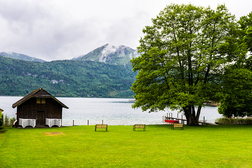 Rain and morning mist on the Wolfgangsee in Austria.  Small well-kept park with benches on a lawn near a lake in Austrian rural landscape. Vintage style