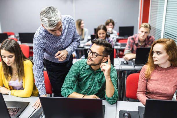 istock Mid adult professor assisting young students during a class at computer lab. 1079586192
