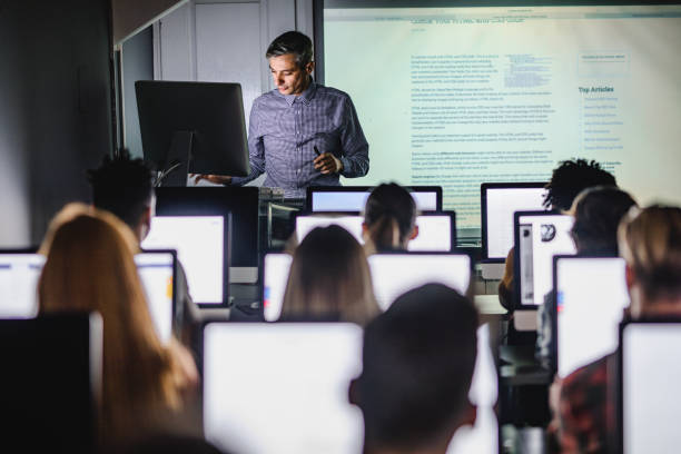 professore adulto medio che insegna una lezione dal pc desktop al laboratorio informatico. - online lesson foto e immagini stock