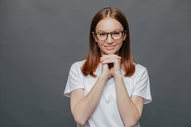 istock Joyful pleasant looking lady keeps both hands under chin, smiles positively at camera, wears optical glasses, casual t shirt, enjoys spare time in good company, isolated over grey background 1079595592