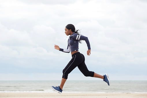Full body side portrait of african american woman running by the beach