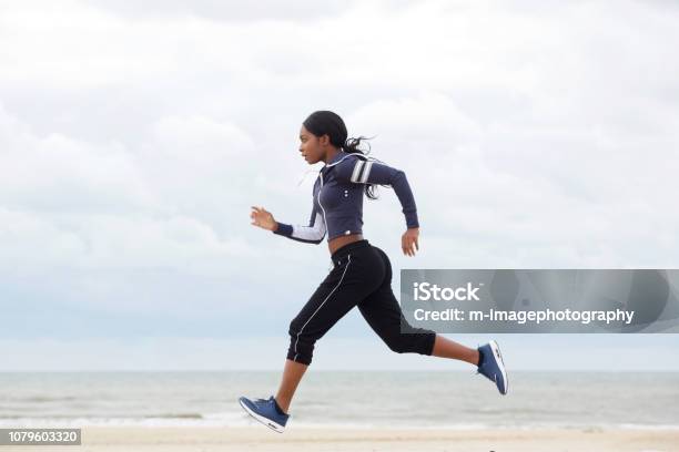 Side Portrait Of African American Woman Running By The Beach Stock Photo - Download Image Now