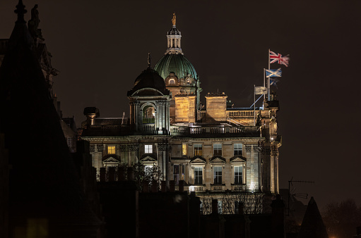 Picture of Old College in Edinburgh taken in the nighttime. The British and Scottish flags are standing on top of the building​.