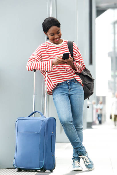 istock young black woman standing with suitcase and looking at mobile phone while waiting at the airport 1079653948