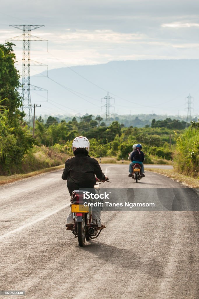 Motorcycle travels on the National Highway T 16 from Salavan to Pakse, Laos. Asphalt road on Bolaven Plateau at evening, Laos people returning home after work. Summer season. Transportation. Asia Stock Photo