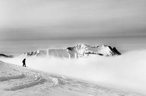 Black and white silhouette of snowboarder on off-piste slope with newly fallen snow and mountains in fog