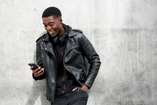 Portrait of happy black man in leather jacket looking at mobile phone