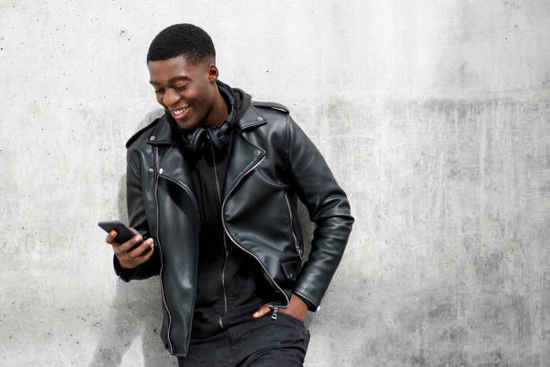 happy black man in leather jacket looking at mobile phone - casaco de couro imagens e fotografias de stock