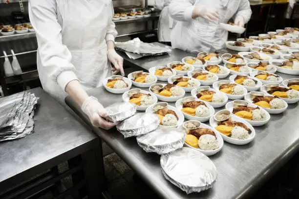 Female cooks are wrapping airline food in foil, commercial kitchen, reality shot, toned image