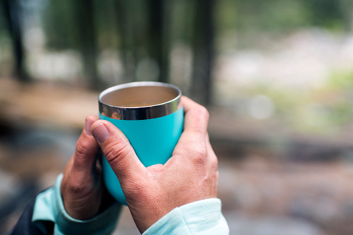 Female hands holding a thermo cup in the forest