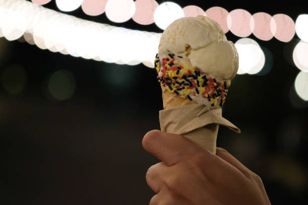 рука проведения ванильного мороженого с bokeh света и размыты в ночное время - melting ice cream cone chocolate frozen стоковые фото и изображения