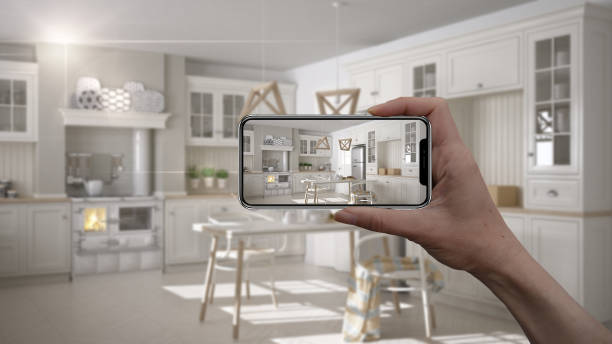 istock Hand holding smart phone, AR application, simulate furniture and interior design products in real home, architect designer concept, blur background, scandinavian white kitchen 1079732436