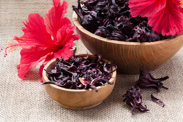 Hibiscus (Roselle, karkade) dry flowers in wooden bowls on burlap background close-up. Healthy organic vitamin herbal tea.