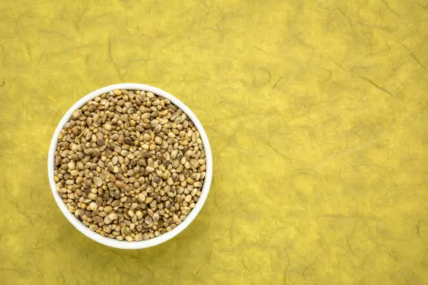 hemp seed in a small ceramic bowl, top view against mulberry paper background