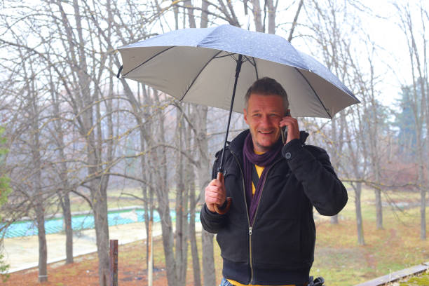 istock Handsome adult man outdoors on rainy autumn day using mobile phone 1079755324