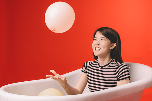 asian chinese female sitting in the bathtub playing with balloon