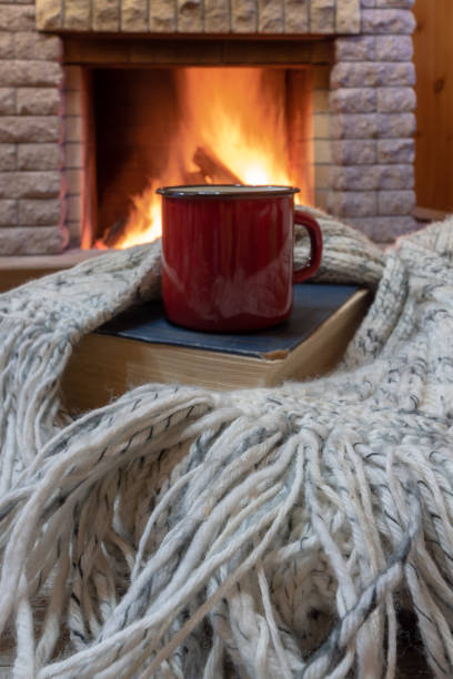 istock Cozy scene before fireplace with red mug with tea, a book, wool scarf. 1079762656