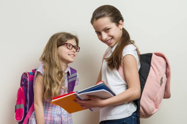 dos chicas sonrientes con bolsas de la escuela. colegialas 7 y 10 años hablando en la escuela - 7 10 years fotografías e imágenes de stock