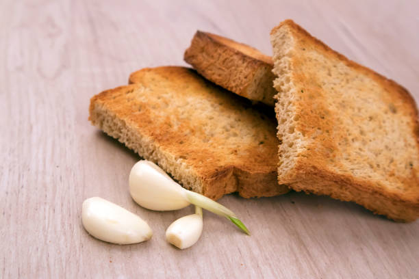 Toasted bread slices with appetite crispy crust and few garlic cloves on wooden board