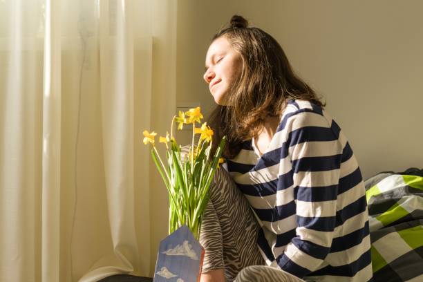 ragazza adolescente con bouquet di fiori di primavera gialli, sorridente e felice seduta a casa a letto - 12 15 months foto e immagini stock