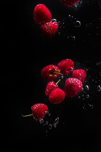 Raspberries falling in water  on a black background. High speed flash splash photography. Fresh raspberries dropped into water. 
Copy space.