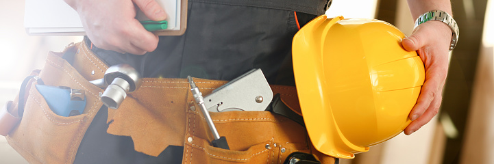 Handyman with hands on waist and tool belt with construction tools against wood background. DIY tools and manual work concept