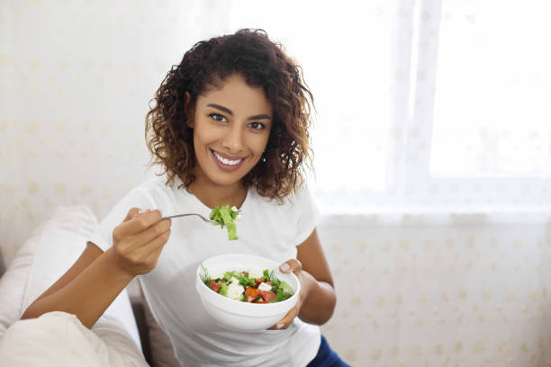 istock Young woman on sofa eating salad 1079794028