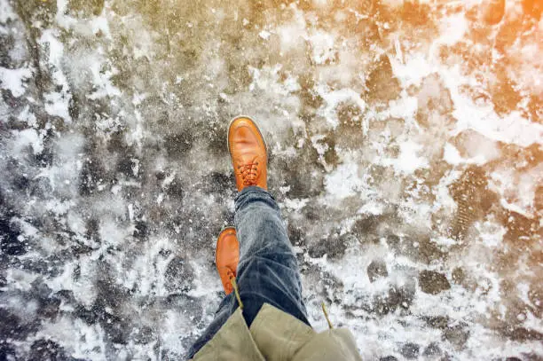 Walk on wet melted ice pavement. First person view on the feet of a man walking along the icy pavement. Pair of shoe on icy road in winter. Abstract empty blank winter weather background
