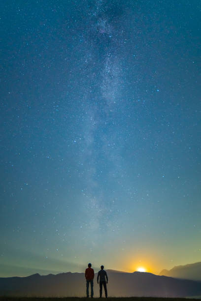 Photo of The two men stand on the background of the milky way. night time