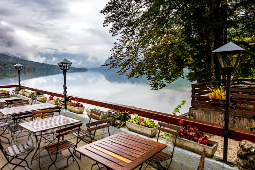 Restaurant cafe wet empty tables chairs beautiful Bohinj lake autumn rainy scenic forest mountains vivid view, travel Ribčev Laz town, Slovenia tourism.
