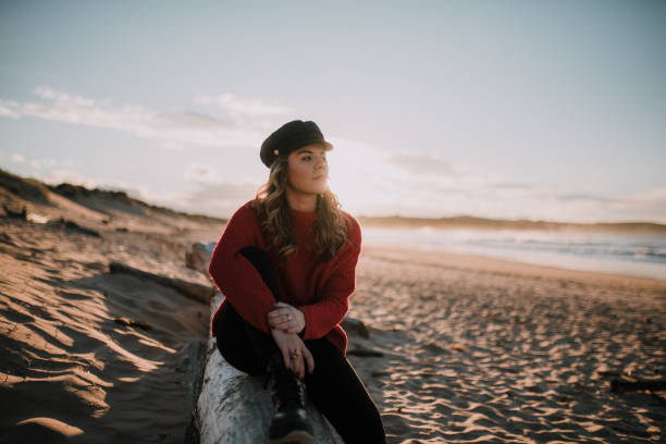 istock Young woman sitting by a beach at sunset in winter 1079837536