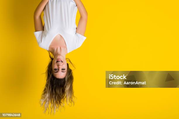 Beautiful Young Blonde Woman Jumping Happy And Excited Hanging Upside Down Over Isolated Yellow Background Stock Photo - Download Image Now