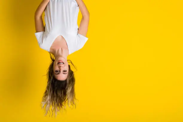Photo of Beautiful young blonde woman jumping happy and excited hanging upside down over isolated yellow background
