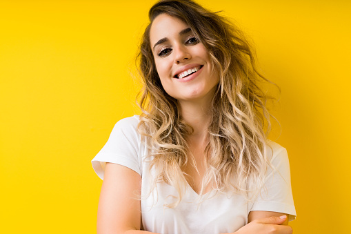 Young beautiful blonde woman over yellow background happy face smiling with crossed arms looking at the camera. Positive person.
