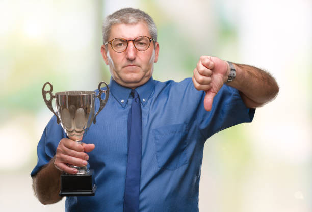 istock Handsome senior successful man holding trophy over isolated background with angry face, negative sign showing dislike with thumbs down, rejection concept 1079856382