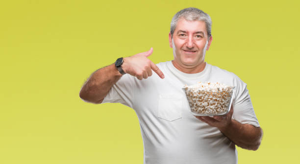 istock Handsome senior man eating popcorn over isolated background with surprise face pointing finger to himself 1079859556