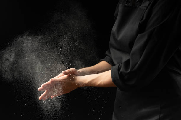 Baker, chef making cotton with flour, freezing flour in the air. Banner, on a black background. Splash of flour. Cooking bread, pasta, sweets and pizza