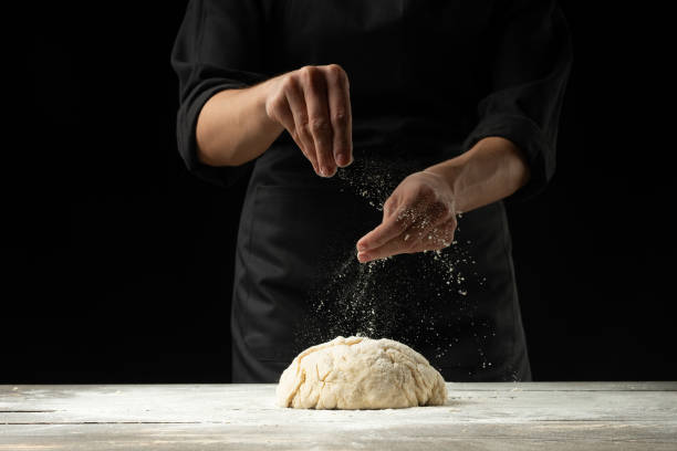 istock A chef in a black apron on a black background prepares Italian pizza, bread or pasta on a black background. Advertising, design for text, menu, recipe book. 1079890324