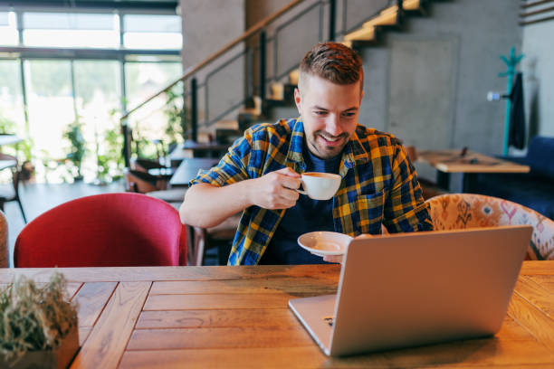 istock Smiling Caucasian male freelancer drinking coffee and looking at laptop while sitting in cafe. Self employing concept. 1079894434