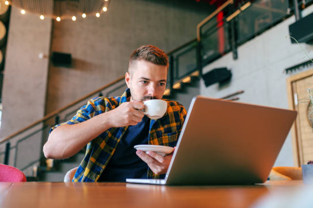 istock Young Caucasian bearded freelancer drinking coffee and looking at laptop while sitting in cafe. Self employing concept. 1079894644
