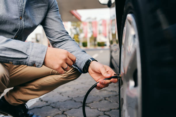 ガソリン スタンドの上にしゃがみとタイヤを膨らませる男のクローズ アップ。 - tire ストックフォトと画像