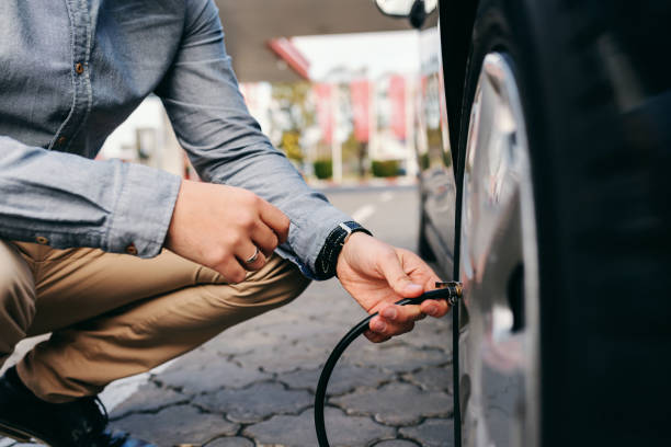 feche de homem agachado no posto de gasolina e inflar o pneu. - encher atividade - fotografias e filmes do acervo