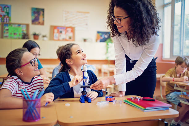 istock Teacher is helping schoolgirl working with a microscope in the classroom 1079928900