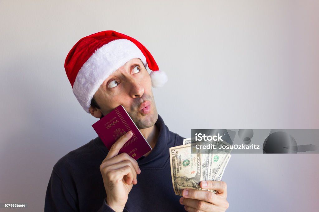Dreamer man on Santa hat holding passport and dollar bills with pensive look Christmas holidays travel escape wish concept. Language translation: European Union, Spain, passport Adult Stock Photo Dreamer man on Santa hat holding passport and dollar bills with pensive look Christmas holidays travel escape wish concept. Language translation: European Union, Spain, passport Adult Stock Photo