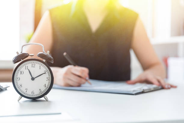 istock Women's hands write in the document. On the table is an alarm clock. 1079938558