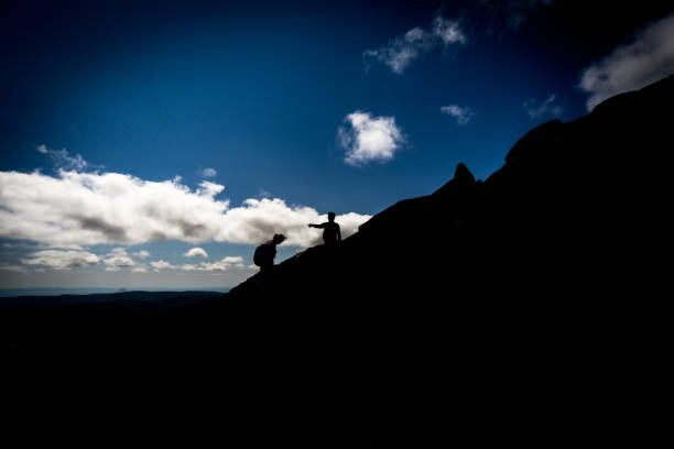 Storm clouds cover the sky as a silhouetted man stands on a hilltop.
