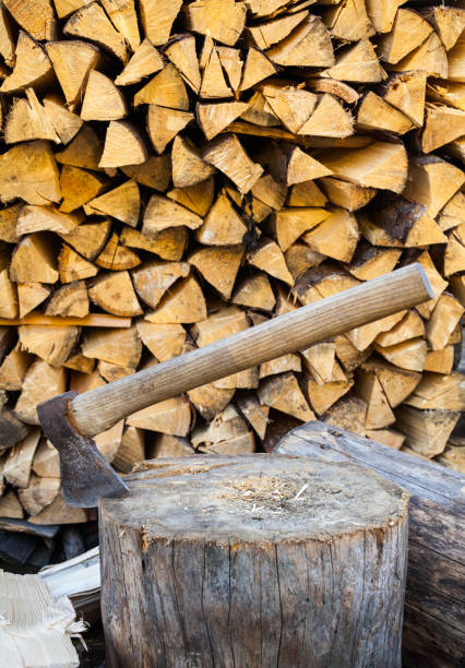 Axe in a stump near the stack of chopped firewood logs. Wood splitting. Close-up.
